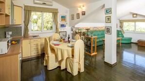 Um quarto aconchegante e bem iluminado, com uma mesa de jantar posta para quatro pessoas, um sofá verde e uma cozinha com armários de madeira e uma janela com cortinas.