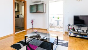 Ein modernes Wohnzimmer mit einem Glastisch, einem Flachbildfernseher und einem Essbereich mit kleinem Tisch und Stühlen.
