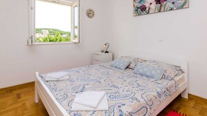 Ein Schlafzimmer mit Bett, Nachttisch, einer Uhr, einem Fenster mit Blick und einem Blumenbild.