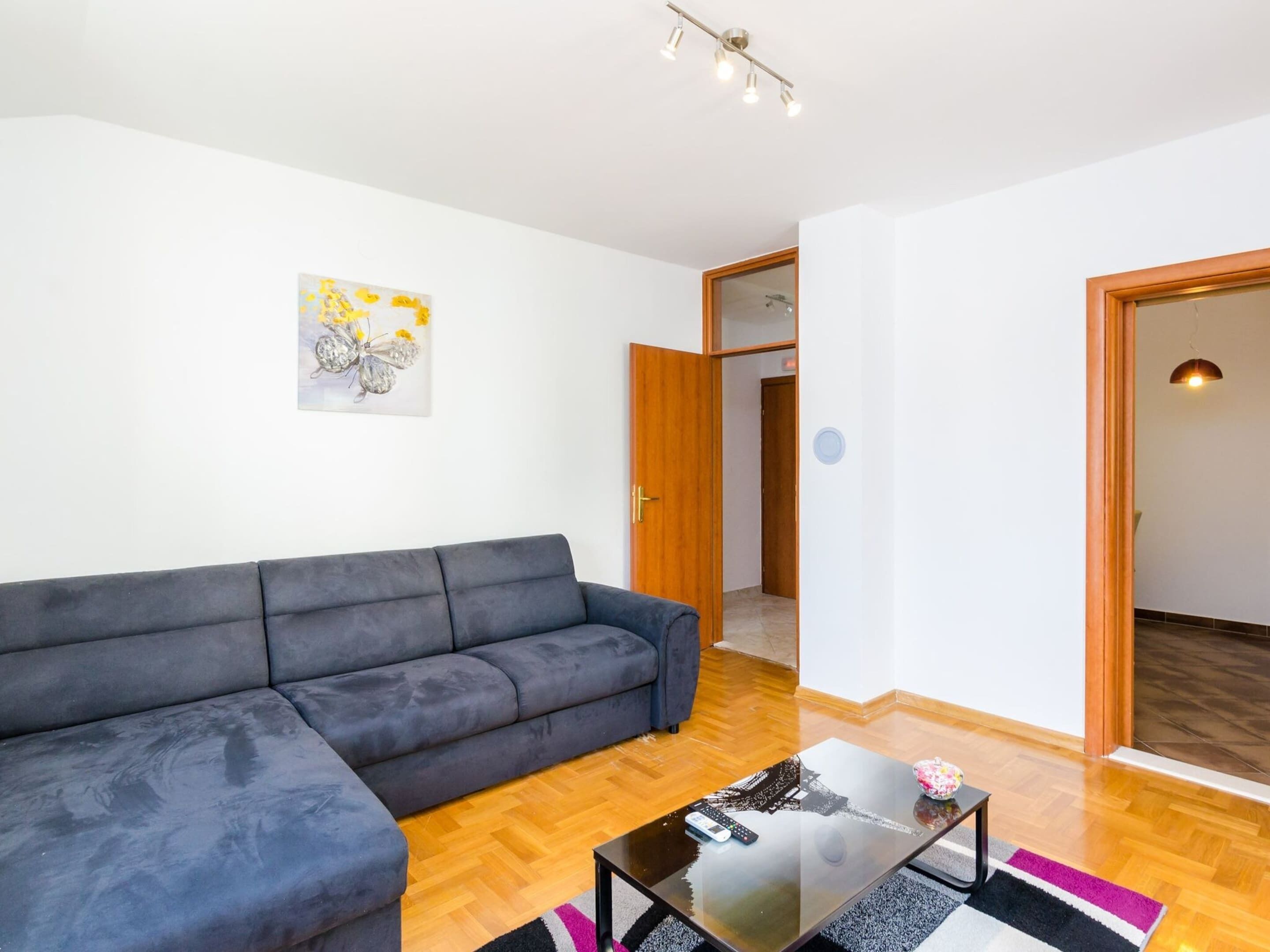 Uma sala de estar moderna com um sofá cinzento, uma mesa de centro de vidro e piso de madeira.
