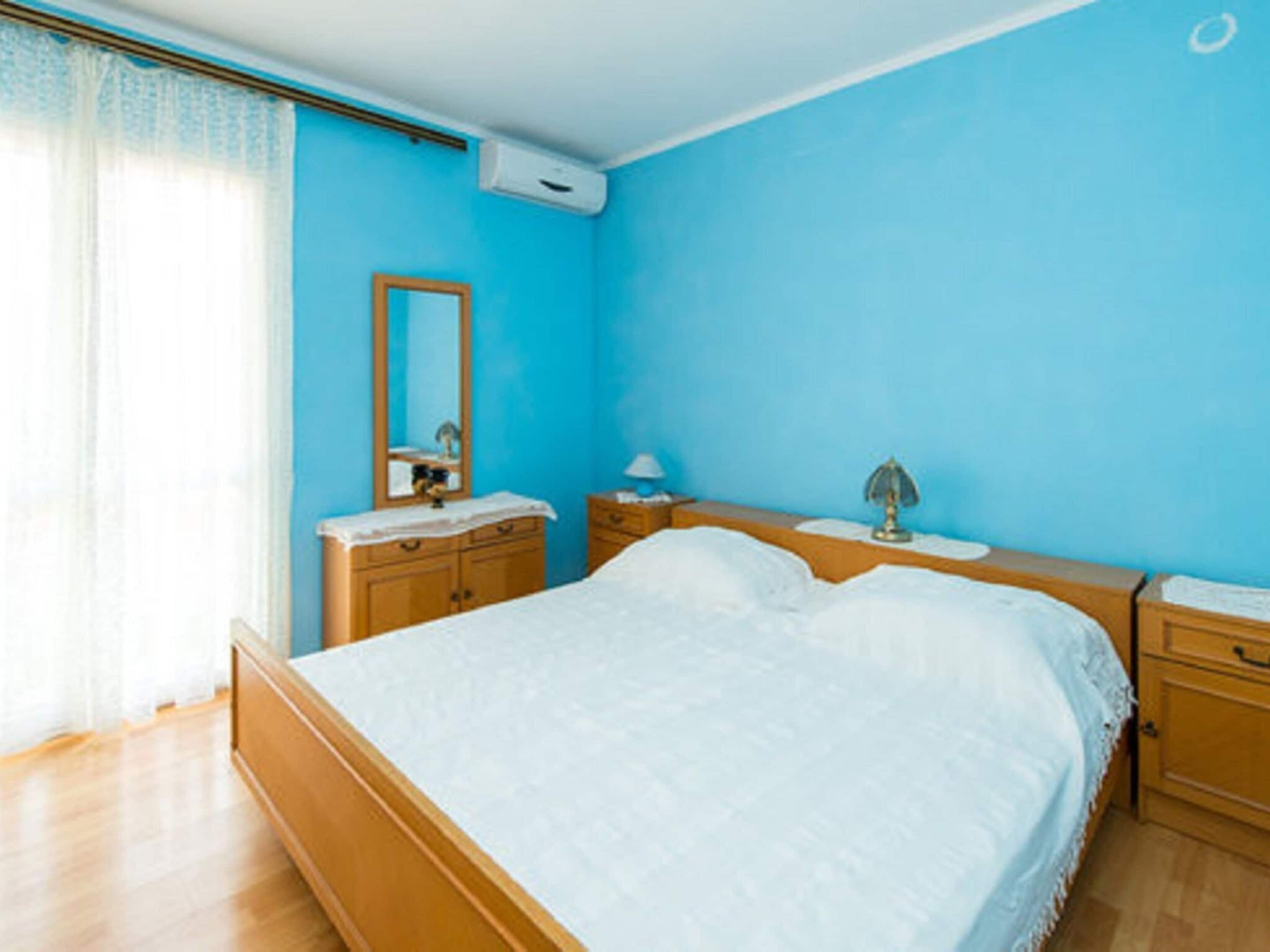 Ein Schlafzimmer mit einem Bett, Nachttischen aus Holz, einem Spiegel und einem Fenster mit Vorhängen.