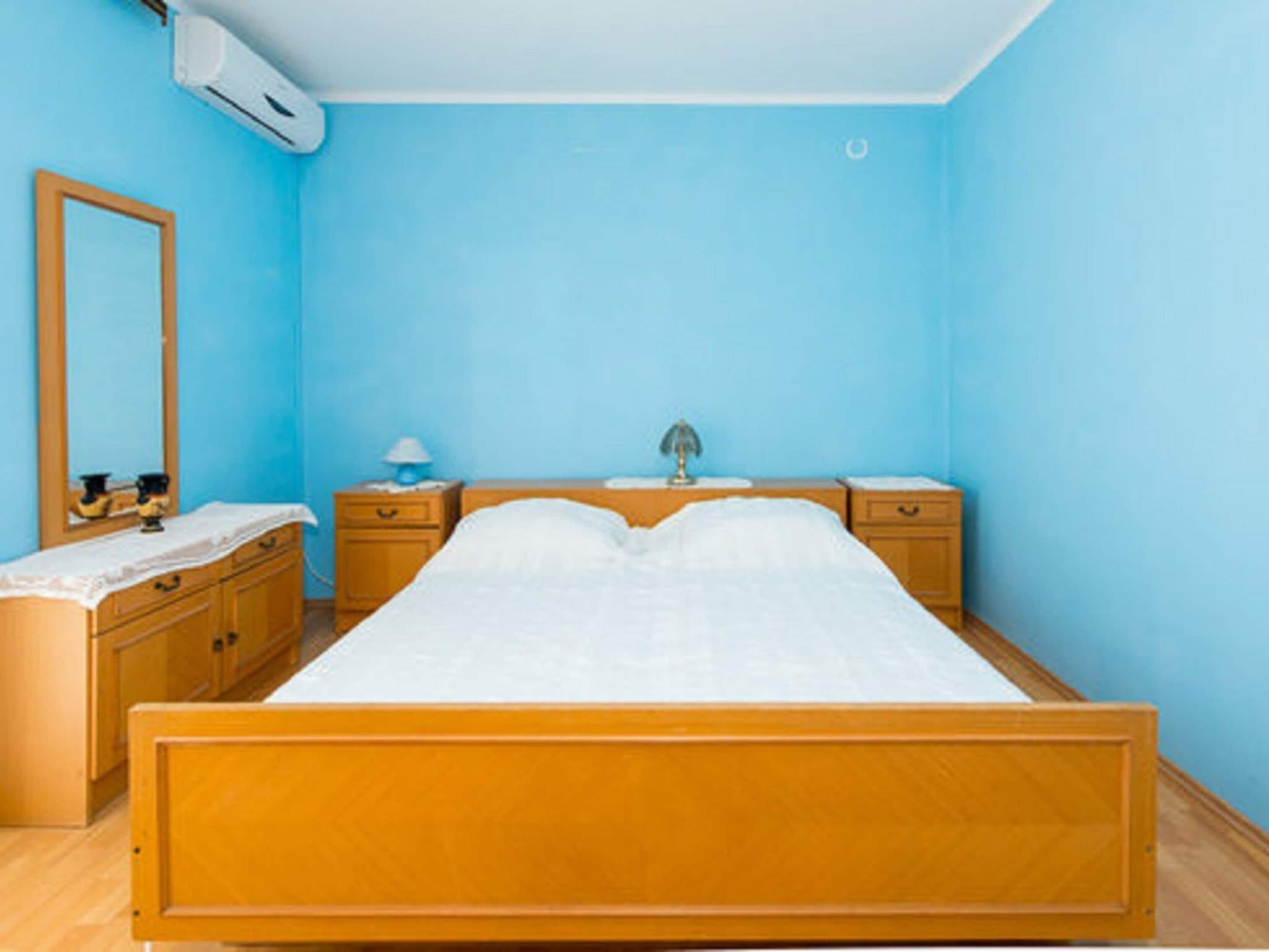 Une chambre à coucher avec un lit en bois, une table de chevet avec une lampe, une commode et un climatiseur fixé au mur.