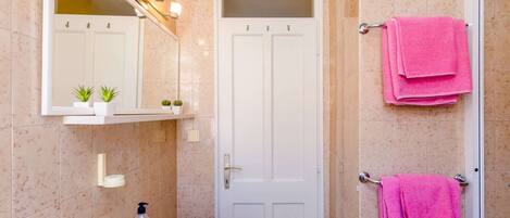 A bathroom with a white sink, a mirror with lights, a door, and pink towels hanging on a rack.