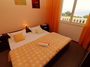 Ein Hotelzimmer mit einem Bett, einem Nachttisch, einer Lampe und einem Fenster mit Blick aufs Meer.