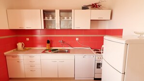 Eine kleine Küche mit weißen Schränken, einem Spülbecken, einem Herd und einem Kühlschrank.