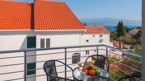Un balcon avec une table dressée pour le petit-déjeuner, un toit recouvert de tuiles rouges et une vue sur la mer et les montagnes.