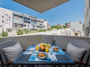 A balcony with a breakfast setup including croissants, fruit, and orange juice. The view includes modern buildings and a clear sky. - Apartment Blue Lagoon - One Bedroom Apartment (Split)