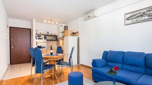 Ein modernes Wohnzimmer mit einem blauen Sofa, einem Esstisch mit Stühlen und einer Küche im Hintergrund.