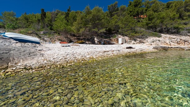 Une plage rocheuse aux eaux cristallines, un bateau et une colline boisée.