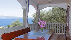 Une table en bois avec un banc, un vase rempli de fleurs violettes et une vue sur la mer et les arbres.
