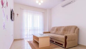 A living room with a beige sofa, a glass-top coffee table, and a large window with white curtains. - Apartment in Medulin With Balconies (Medulin)