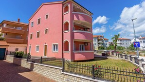 A pink multi-story residential building with balconies, a paved driveway, and a stone wall. - Apartment in Medulin With Balconies (Medulin)