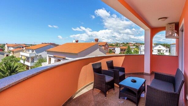 A balcony with wicker furniture, a table, and a view of surrounding buildings. - Apartment in Medulin With Balconies (Medulin)