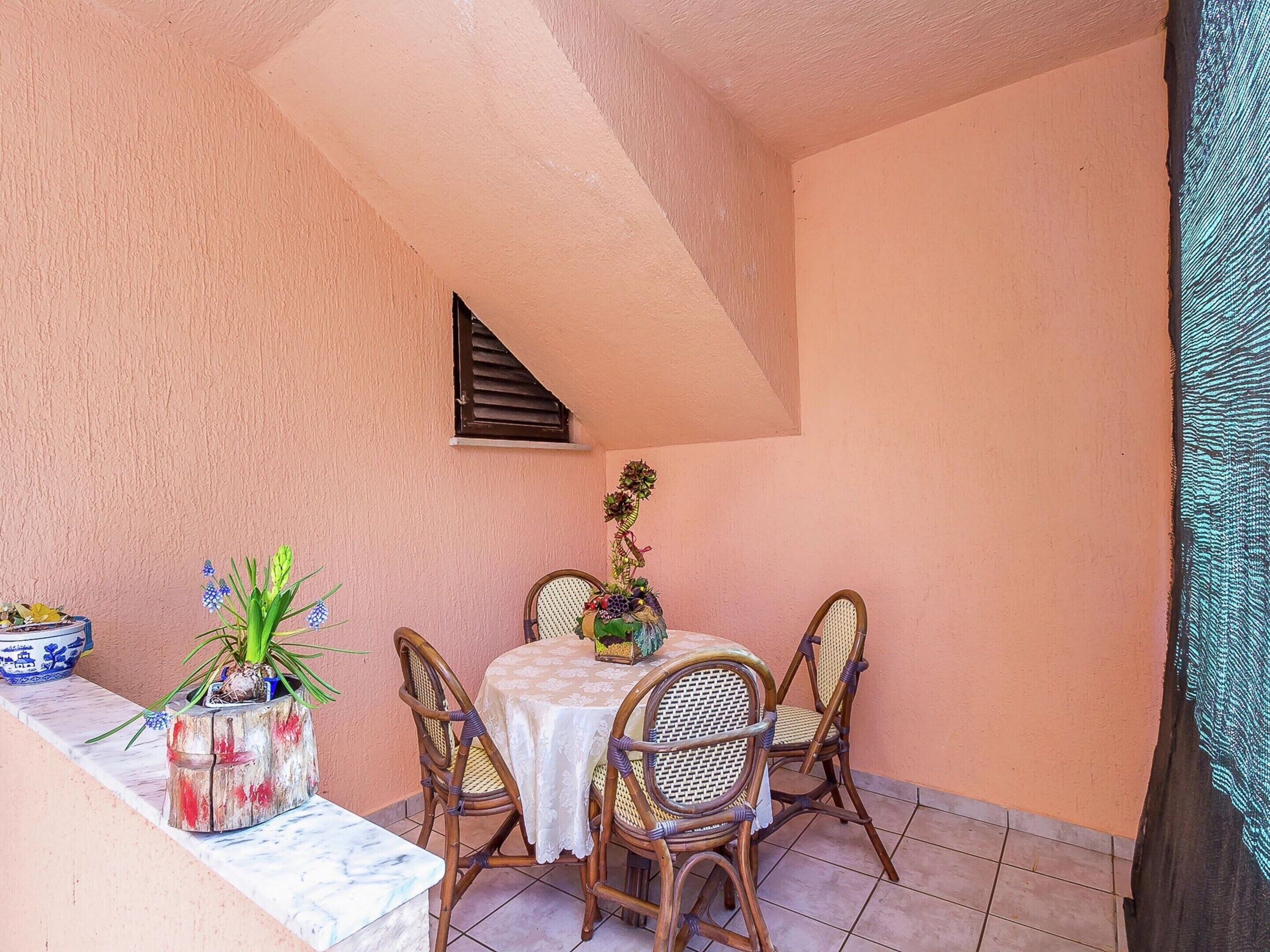 A small patio with a table and four wicker chairs, a potted plant, and a small window.