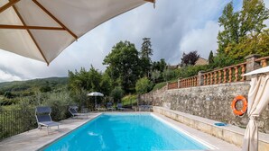 Une piscine entourée de murs de pierre et de verdure, avec des chaises longues et des parasols.