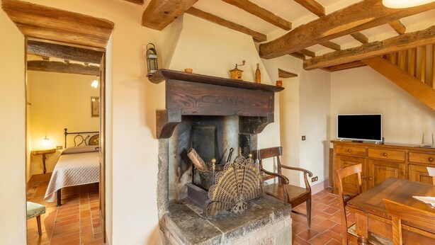 Une pièce rustique avec des poutres apparentes, une cheminée en pierre, une table en bois avec des chaises et un téléviseur posé sur un meuble en bois.