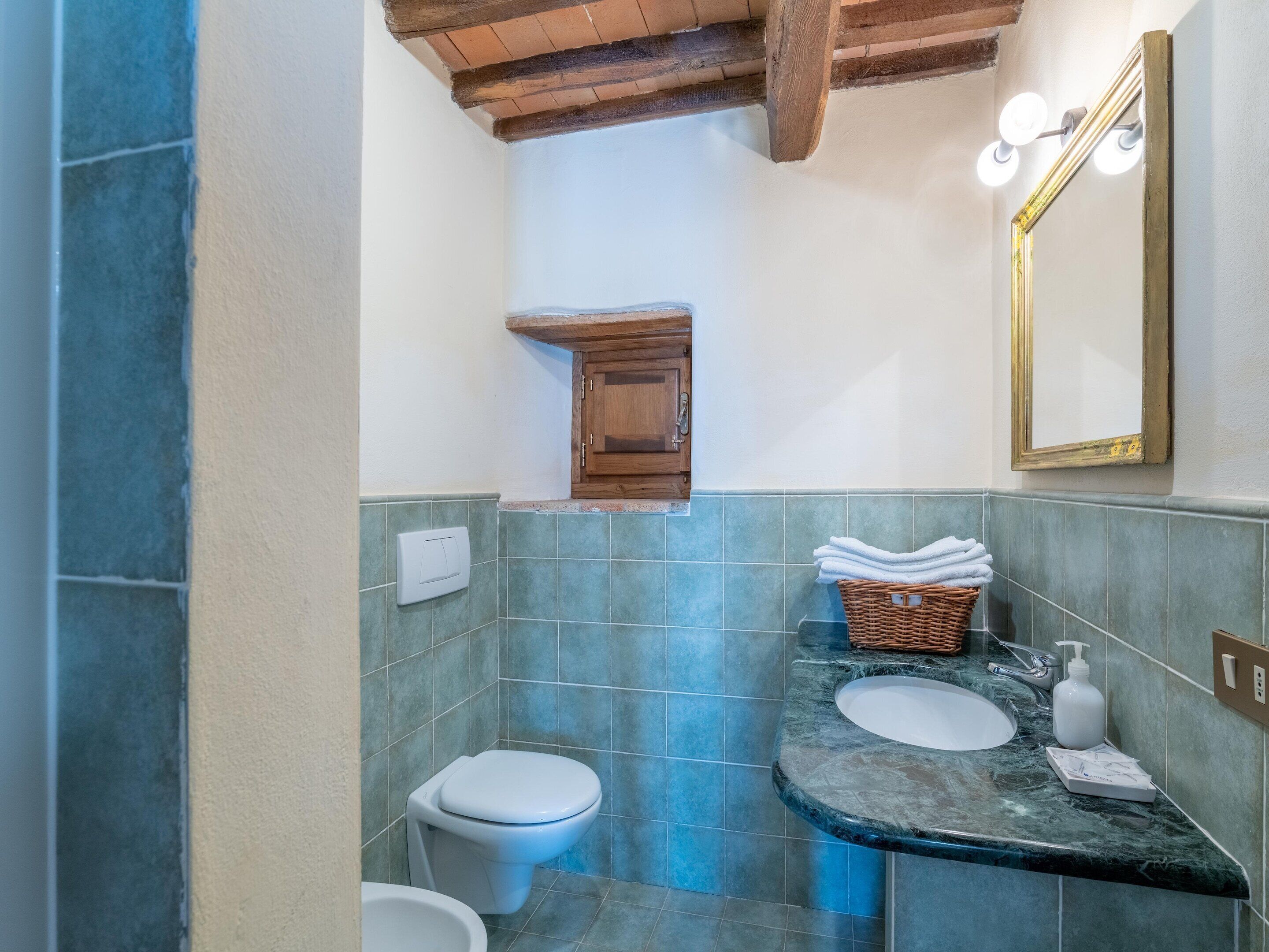 A bathroom with a white toilet, a sink with a marble countertop, a wicker basket with towels, and a wooden cabinet.