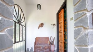 Un hall d’entrée au sol en pierre, avec un banc en bois, une lanterne et une porte ornée d’un rideau à motifs de tournesols.