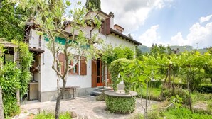 Une maison traditionnelle dotée d’un patio en pierre, entourée d’une végétation luxuriante et d’un petit jardin.
