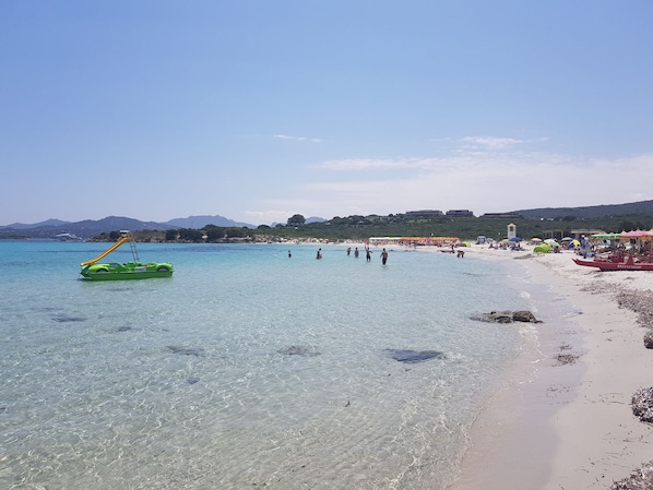 A beach with clear water, a green inflatable boat, and beach umbrellas.