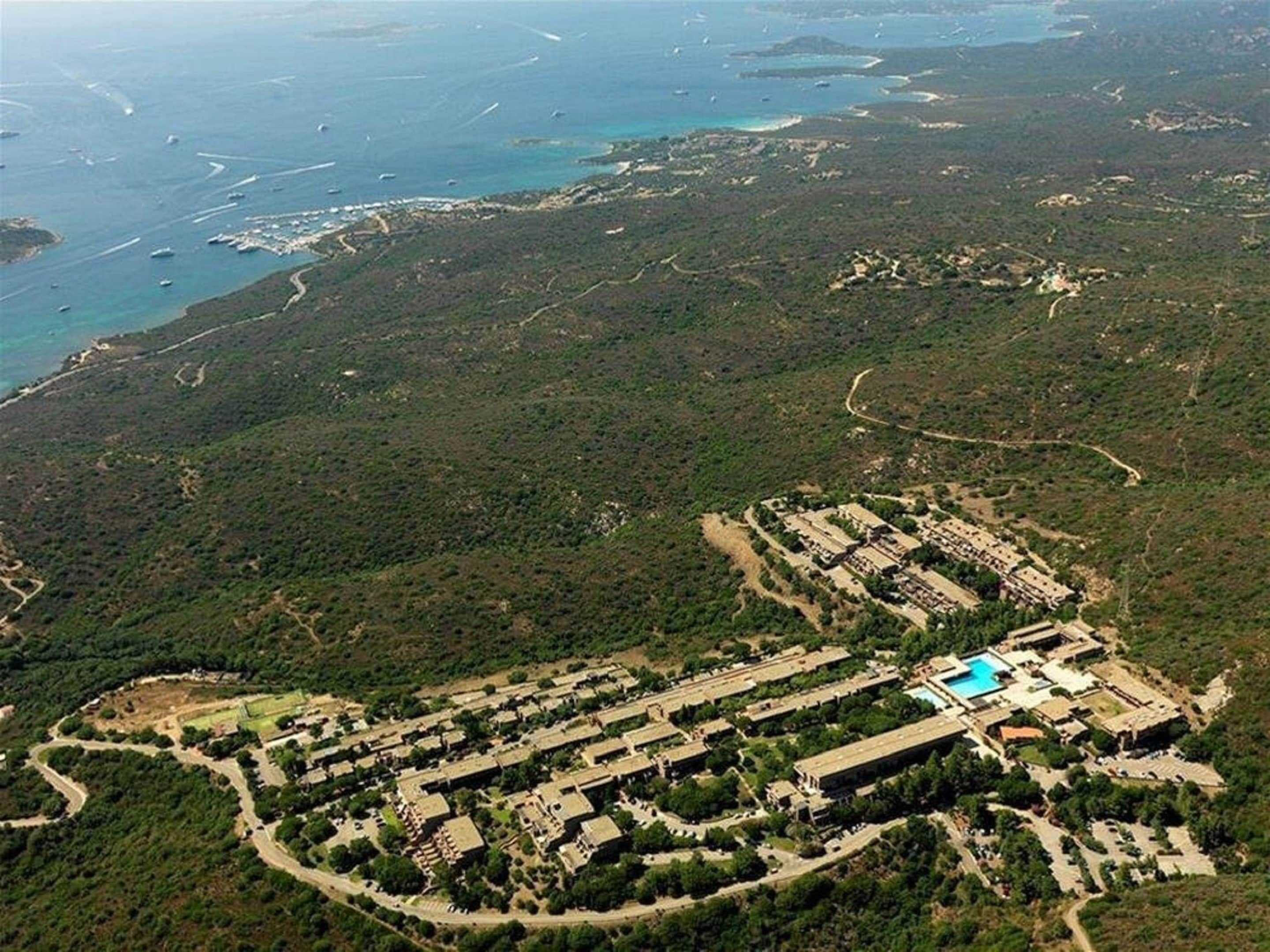 An aerial view of a resort with multiple buildings, a swimming pool, and surrounding natural landscape.