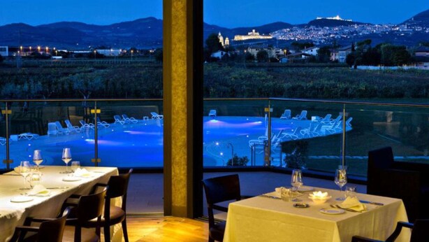 Un restaurante con mesas dispuestas para comer, con vistas a una piscina y al paisaje urbano de noche.