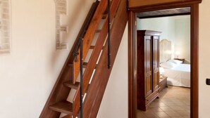 Una escalera de madera que lleva a un dormitorio con cama, mesita de noche y armario.
