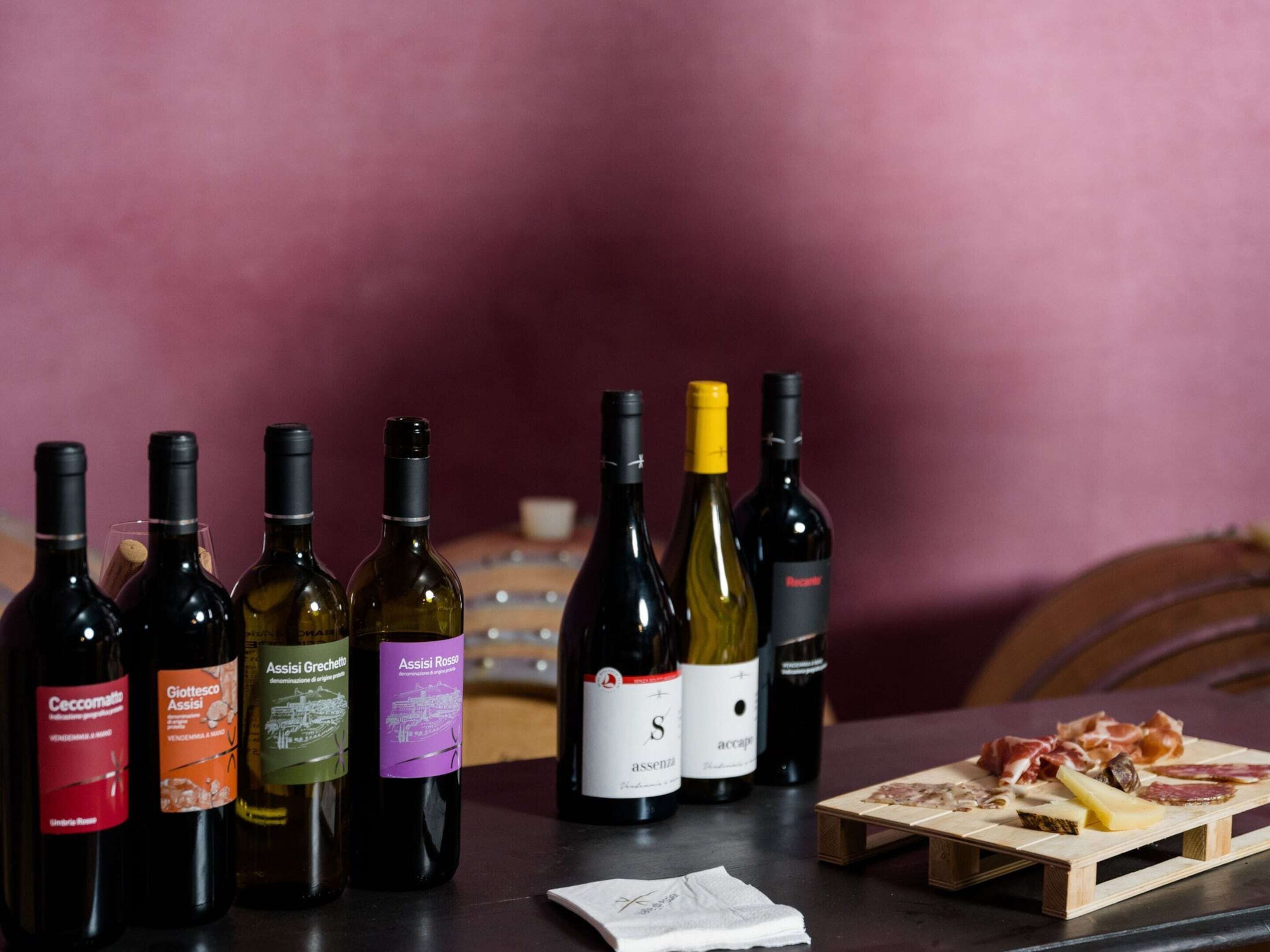A selection of wine bottles and a cheese board with various meats on a wooden table.