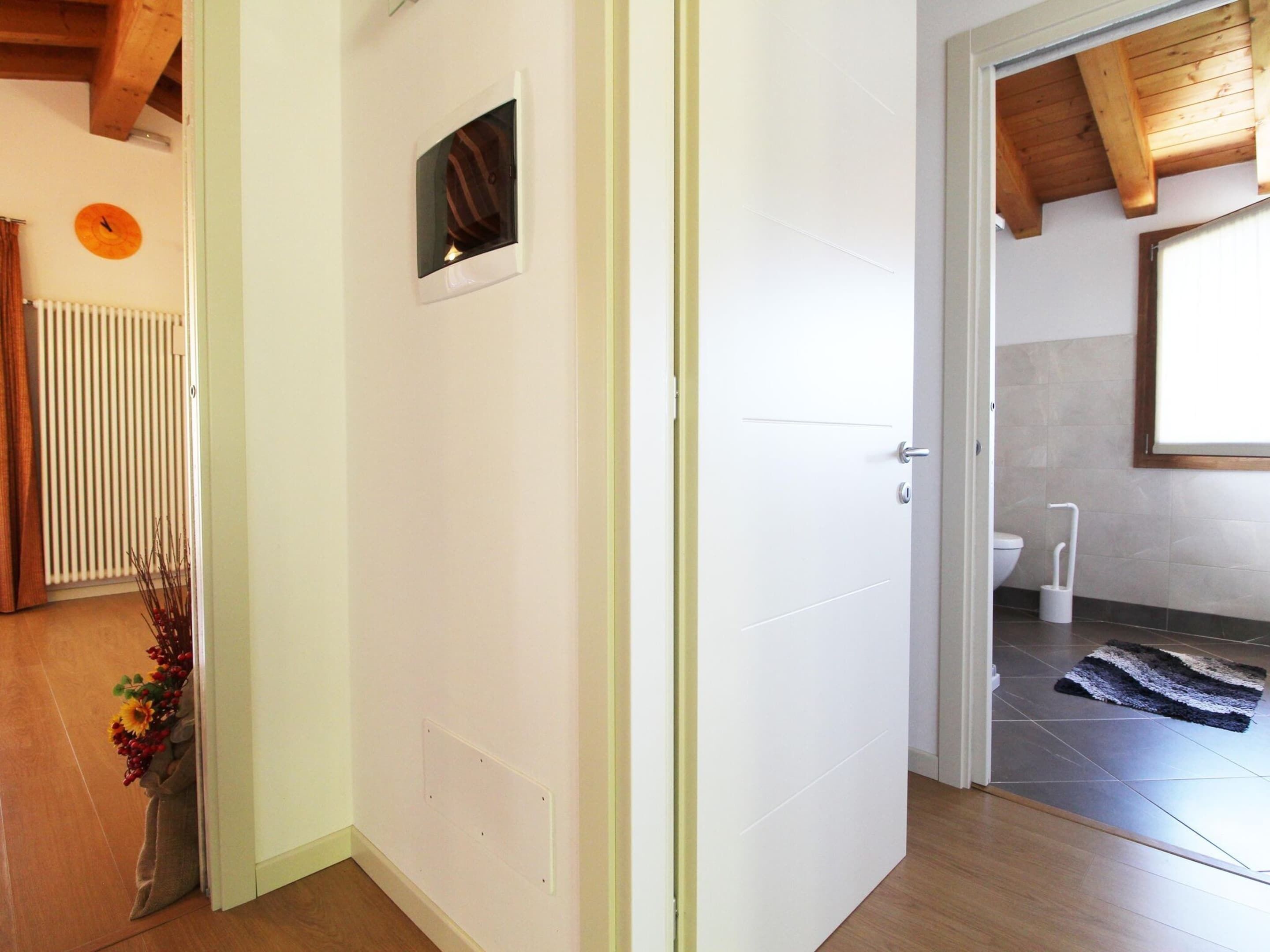 A hallway with a white door, a radiator, a clock, and a window with a view of a bathroom.