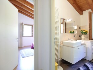 A modern bathroom with a white vanity, a mirror, a towel rack, and a washing machine. - Belvilla by OYO Riva dei Tor (Miane)