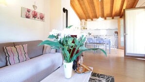 A living room with a sofa, a coffee table with a plant, and a dining area with a table and chairs. - Belvilla by OYO Riva dei Tor (Miane)