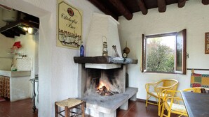 A rustic interior with a stone fireplace, wooden furniture, and a window with a view of greenery. - Mountain Hideaway for Four (Santa Giustina)