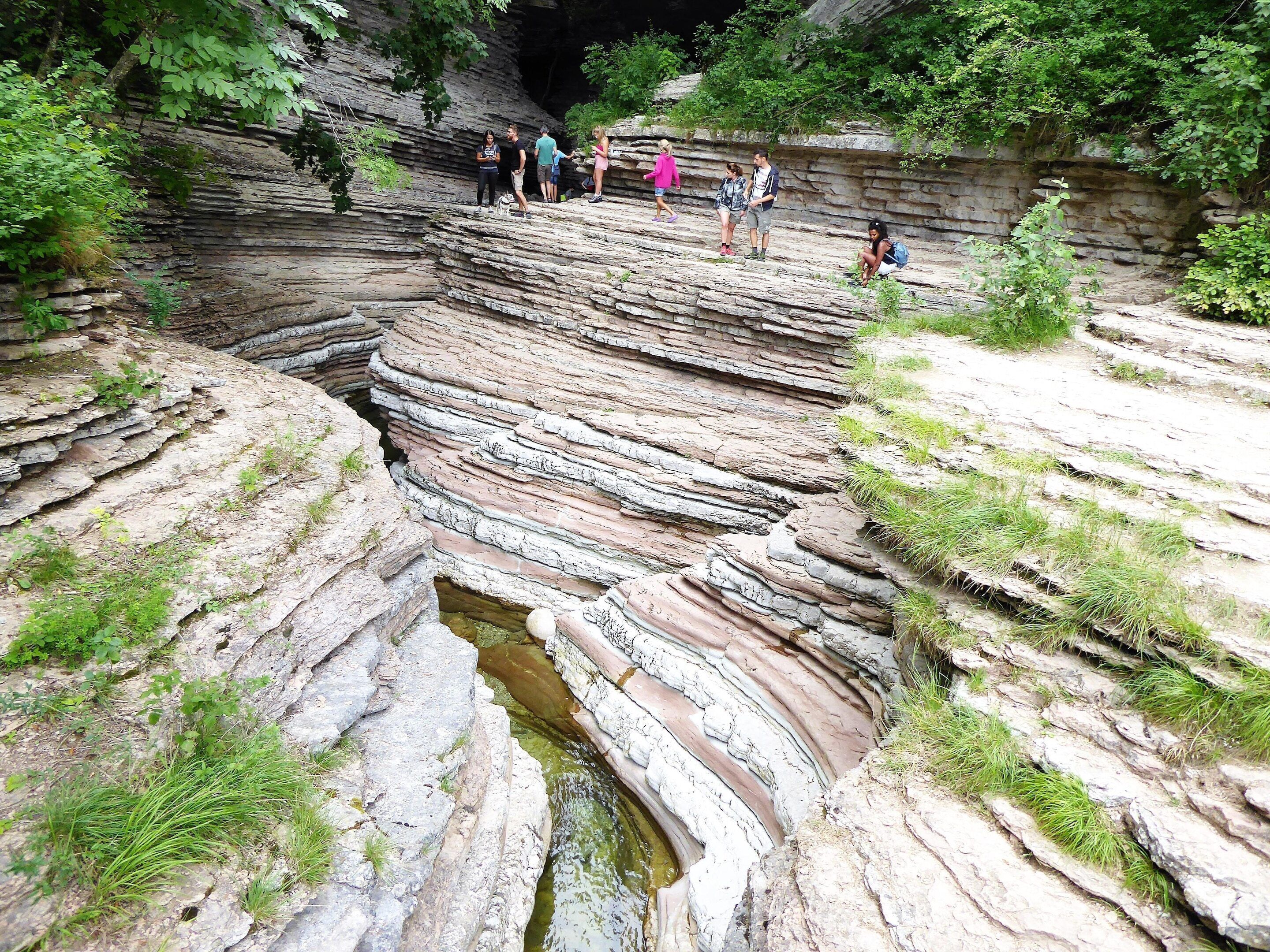 A natural rock formation with layered strata and a small water body at its base.