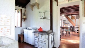 A rustic kitchen with a white stove, a red kettle, and a vintage stove. There is a wooden table with chairs in the background. - Mountain Hideaway for Four (Santa Giustina)