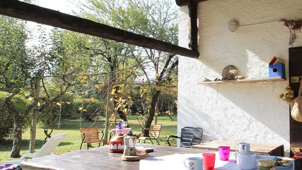 An outdoor dining area with a table set for two, surrounded by chairs, and a view of a garden with trees and grass. - Mountain Hideaway for Four (Santa Giustina)