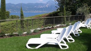 Een rij witte lounge stoelen op een gazon met uitzicht op bergen en een wateroppervlak.
