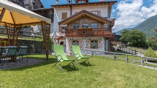 Een chalet met een stenen gevel, houten balkons en een gazon met terrasmeubilair.