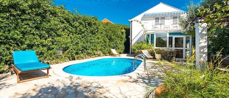A swimming pool with lounge chairs, a stone patio, and a white building with a blue roof.
