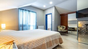 A modern hotel room with a large bed, a desk with a lamp, a chair, and a view of a cityscape through the window. - Villa Piano - Four Bedroom Villa With Terrace and Swimming Pool (Zupa dubrovacka)
