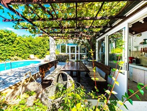 Un espace extérieur aménagé, abrité et doté d'une piscine, de meubles en osier et offrant une vue sur la verdure.