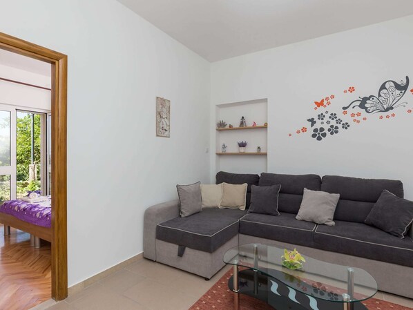 Een moderne woonkamer met een grijze modulaire bank, een glazen salontafel en uitzicht door een groot raam.