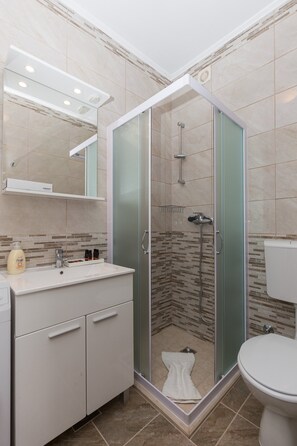 Een moderne badkamer met een douchecabine van glas, een witte wastafel en een toilet.