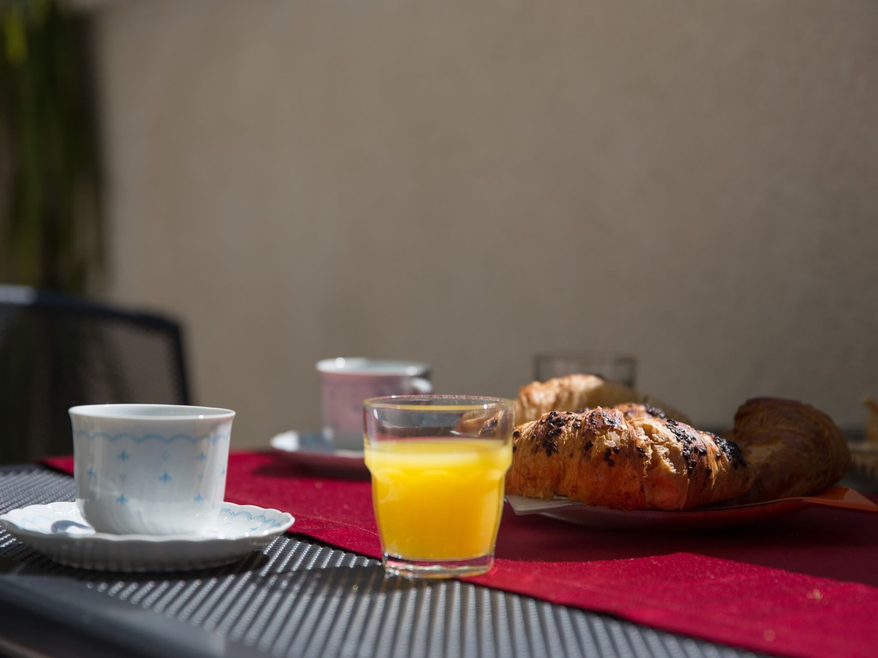 A table with a croissant, a glass of orange juice, and a small cup on a red tablecloth.