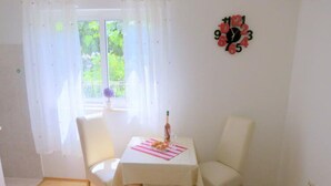 A small dining area with a table and two chairs, a window with curtains, and a wall clock. - Apartments Franka - Studio With Terrace and Sea View (Dubrovnik)