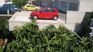 A red car parked on a concrete surface with greenery in the foreground. - Apartments Franka - Studio With Terrace and Sea View (Dubrovnik)