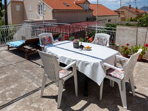 Um pátio com mesa e cadeiras, cercado por plantas em vasos e um corrimão.