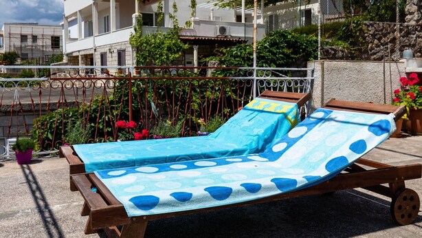 A wooden sun lounger with a blue and white polka dot cover, positioned on a balcony with a stone wall and potted plants in the background. - Apartments Franka - Studio With Terrace and Sea View (Dubrovnik)