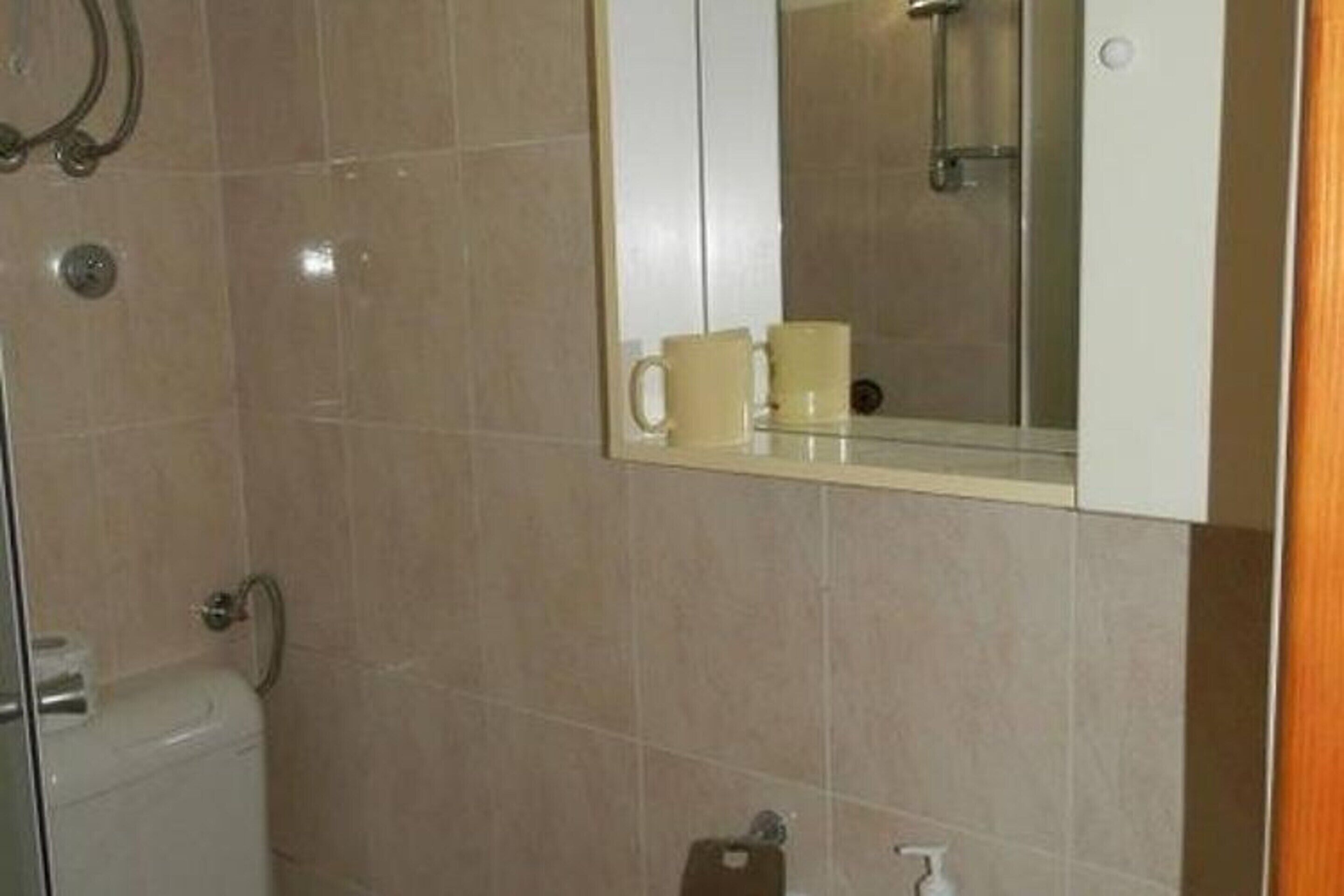 A bathroom with a toilet, a sink, a mirror, and a shelf with two cups.