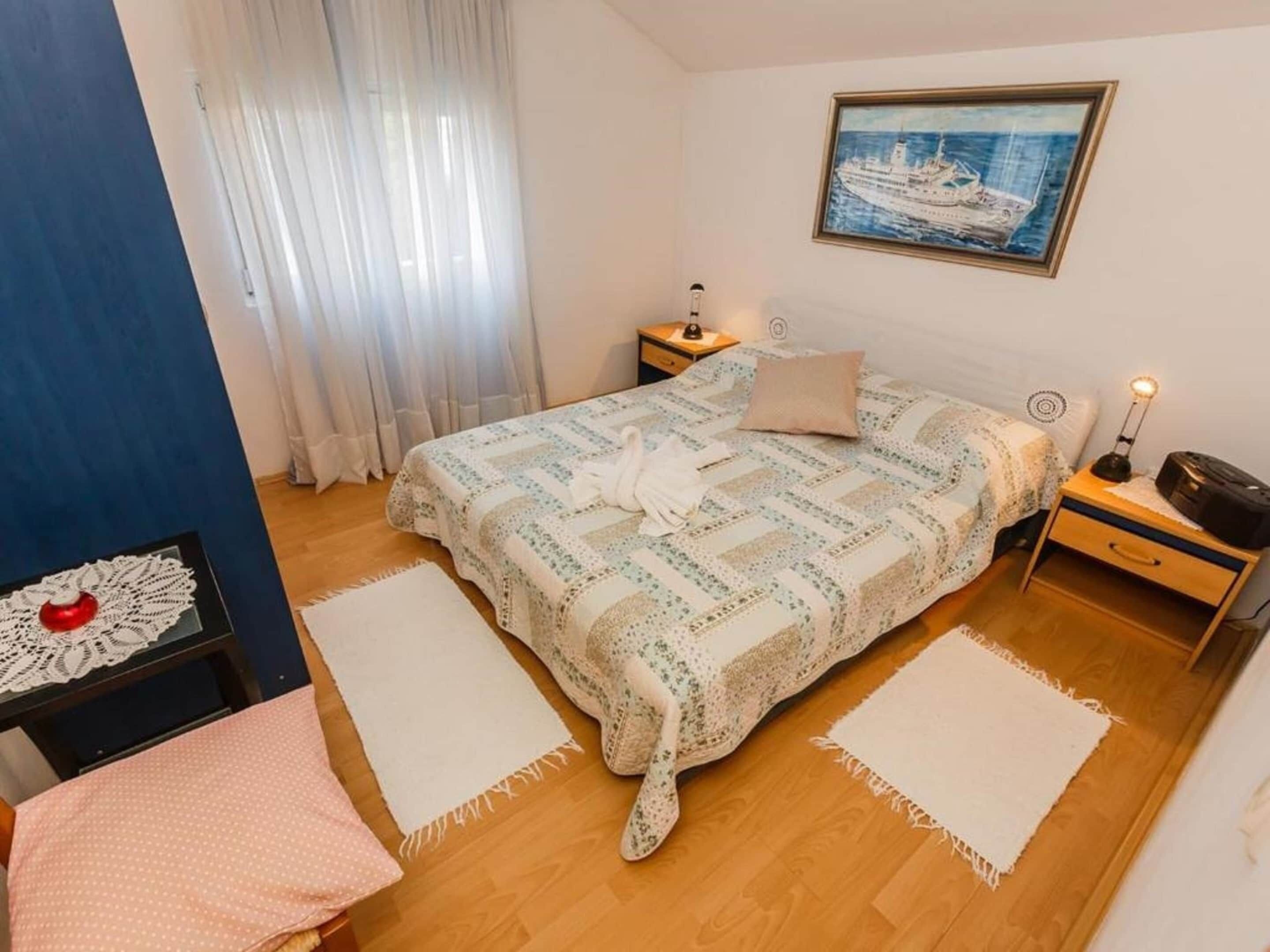 Una camera da letto con un letto, un comodino, una lampada, un quadro appeso e una finestra con tende.