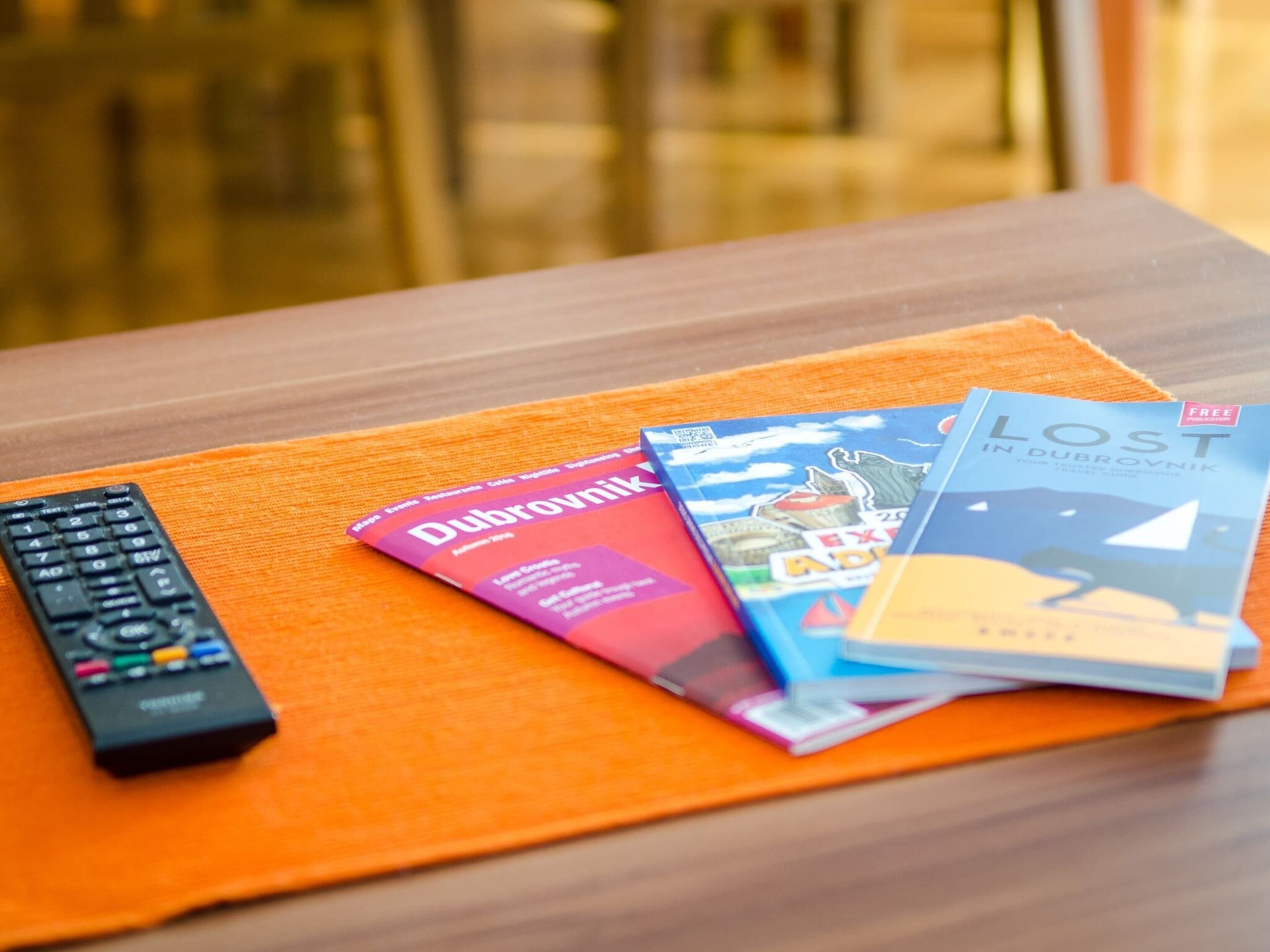 A remote control, a magazine titled 'Dubrovnik', and a book titled 'Lost in Dubrovnik' on an orange mat.